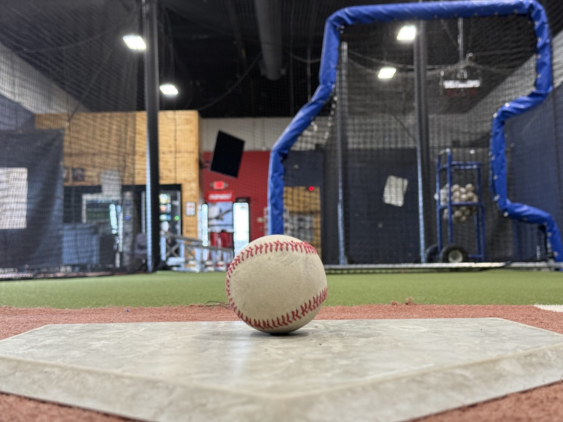 A baseball resting on home plate inside the @BAT Elite indoor facility
